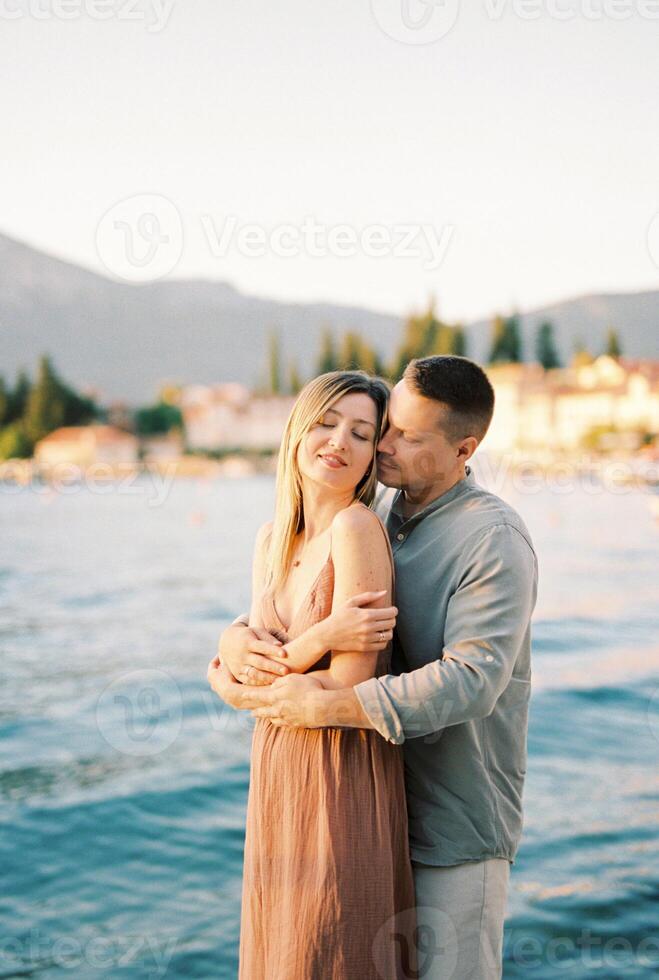 homem abraços mulher a partir de atrás enquanto em pé em a Beira Mar foto