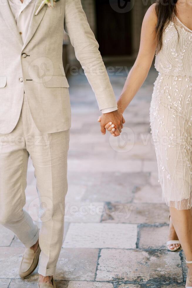 noiva e noivo andar segurando mãos ao longo a pavimentação pedras. cortado. sem rosto foto
