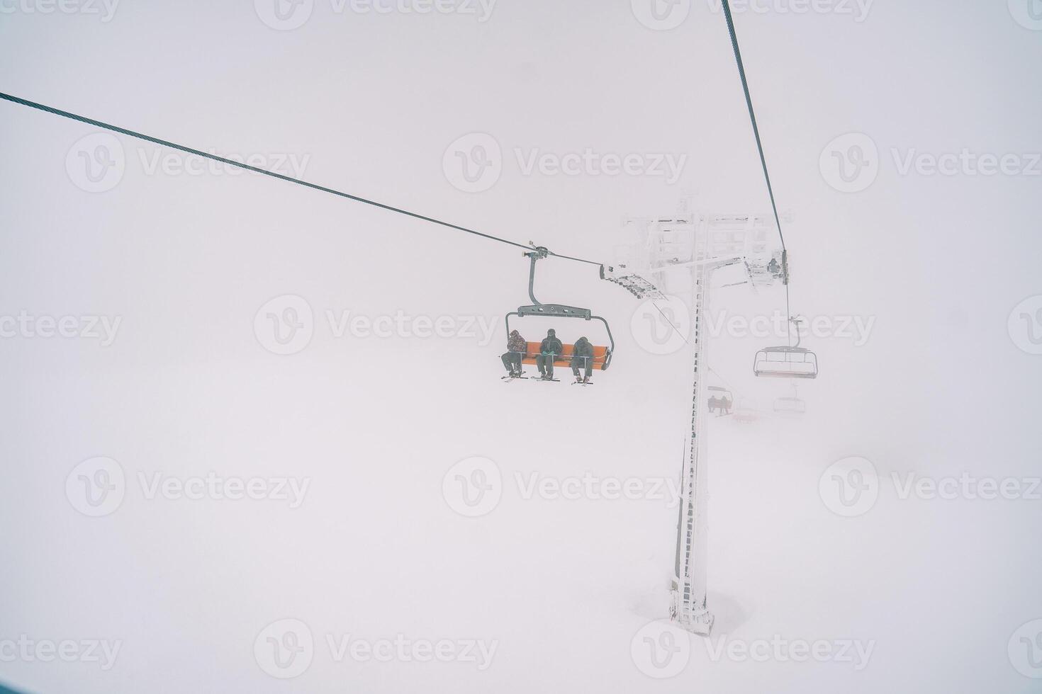 esquiadores em uma quatro lugares teleférico passeio acima a montanha através a névoa foto