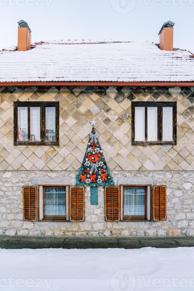 sentido Natal árvore com vermelho arcos e guirlandas em a fachada do uma duas histórias casa com uma coberto de neve cobertura foto