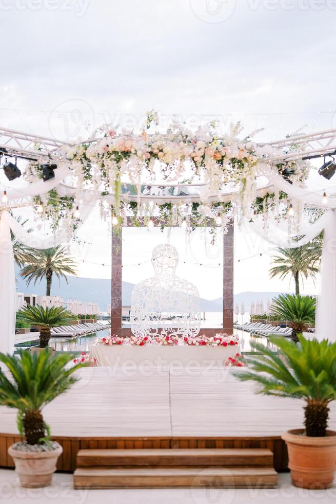 etapa com uma volta marquise decorado com flores perto uma vime escultura perto uma quadrado quadro, Armação dentro uma natação piscina foto