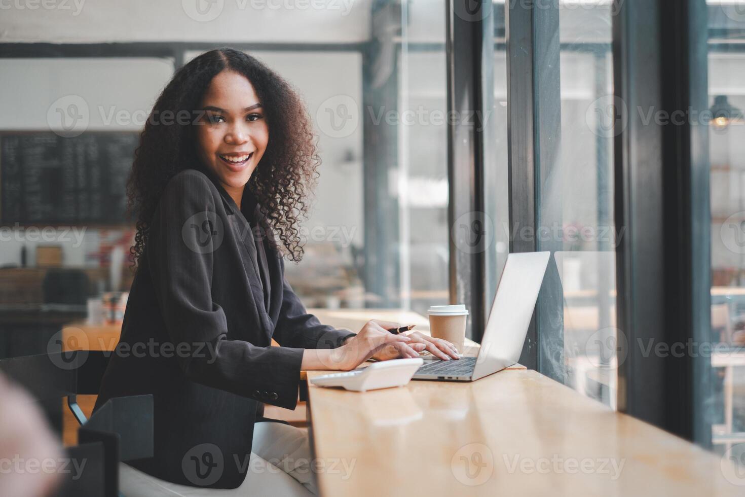 com uma brilhante sorriso, uma jovem empresária é absorta dentro dela trabalhos em uma computador portátil às uma cafeteria, dela positivo energia Coincidindo a animado ambiente por aí dela. foto