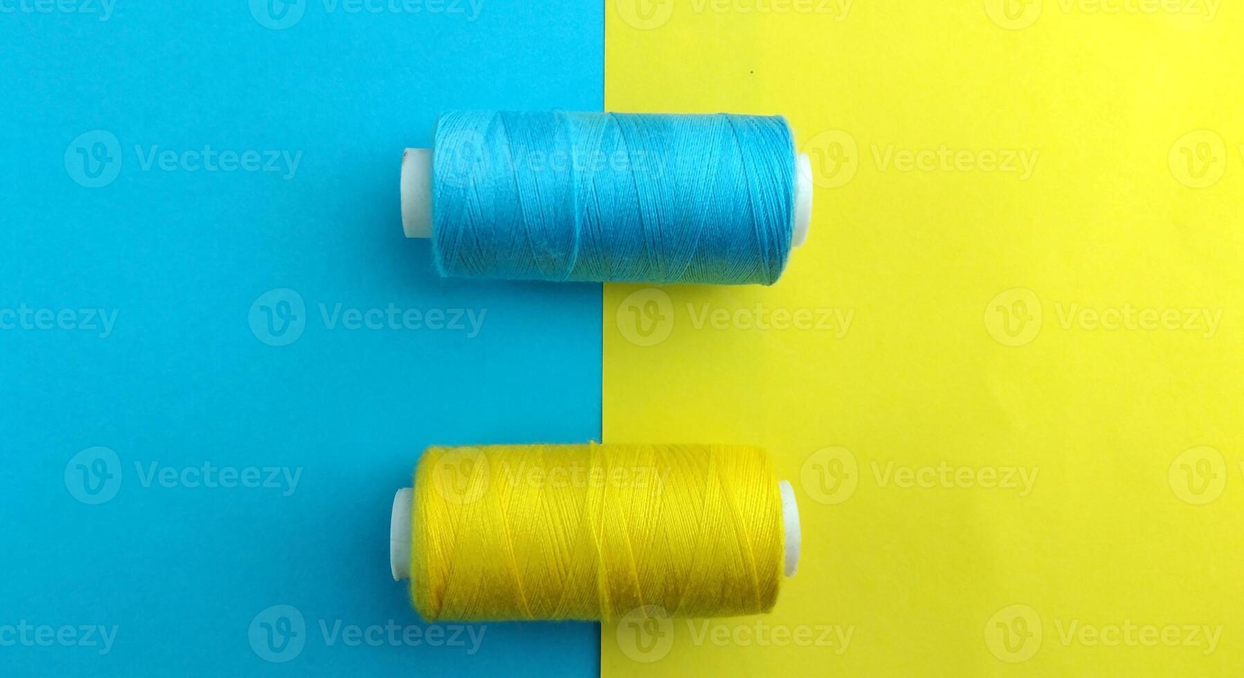 carretéis do fio e uma agulha em uma amarelo e azul fundo, contraste consept foto