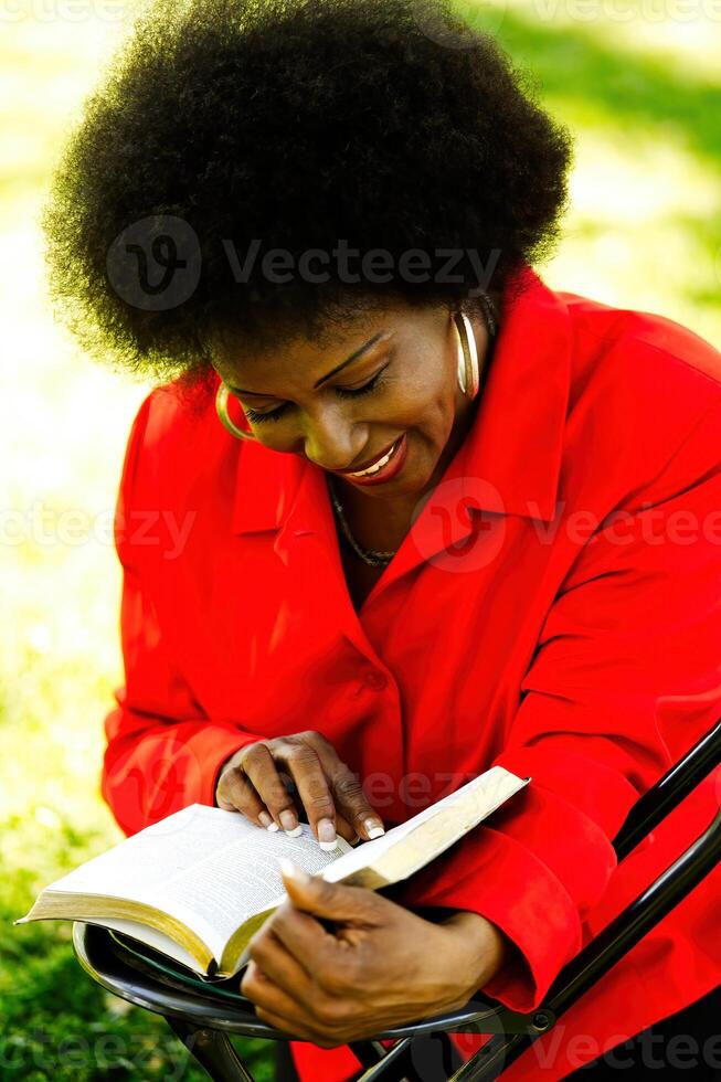 meio envelhecido africano americano mulher sentado ao ar livre lendo foto