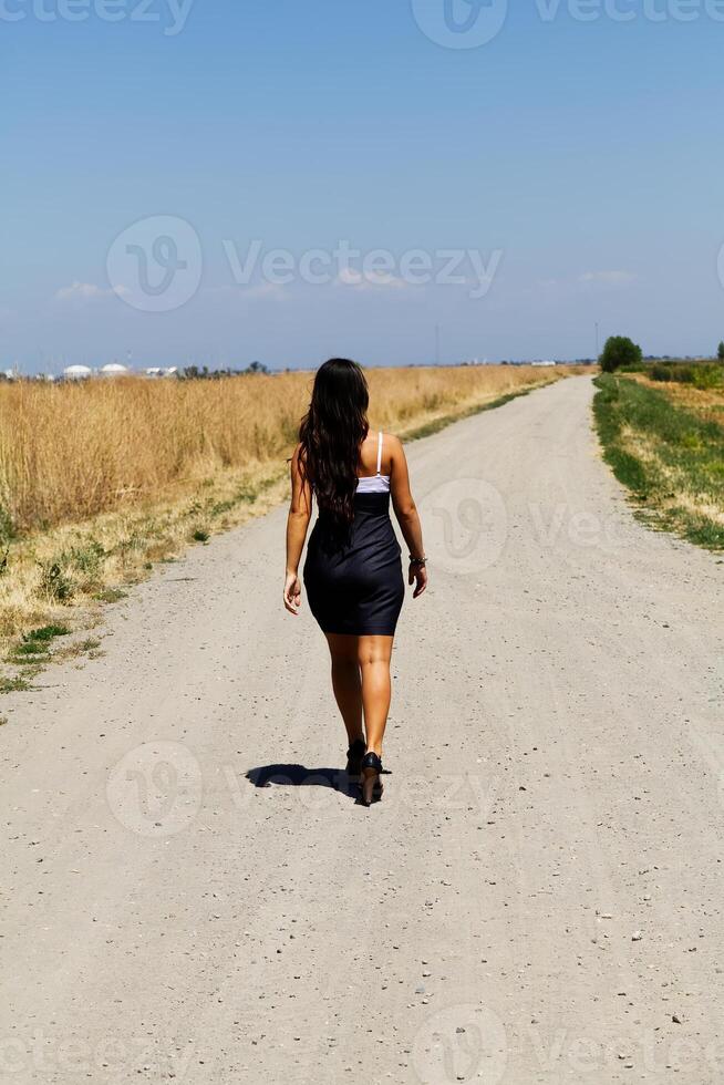 jovem adolescente caucasiano menina caminhando baixa cascalho estrada dentro vestir foto