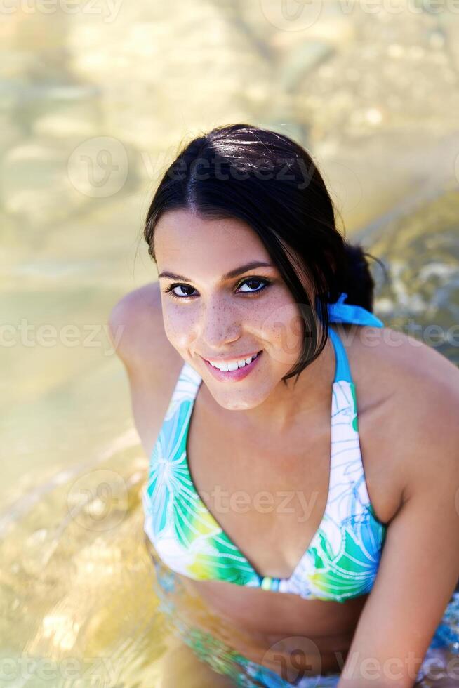 sorridente caucasiano mulher dentro azul bikini sentado dentro rio foto