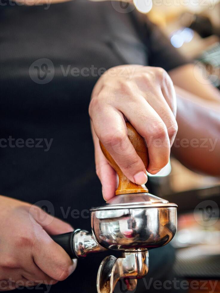 mão do uma barista segurando uma portafilter e uma café violar fazer a espresso café. barista prensas terra café usando uma violar dentro uma café fazer compras foto