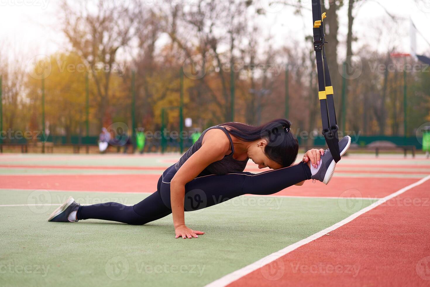 menina atleta funcional Treinamento em campo esportivo. misturado raça jovem adulto mulher Faz exercite-se com suspensão sistema. saudável estilo de vida. alongamento ao ar livre Parque infantil. foto