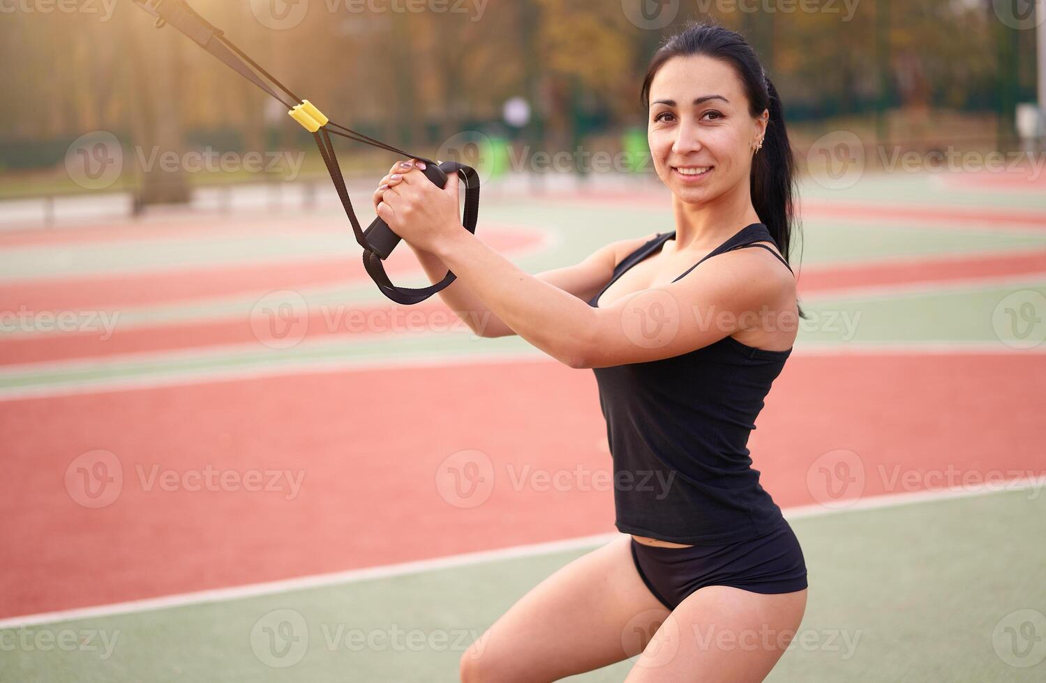 menina atleta Treinamento usando trx em campo esportivo. misturado raça jovem adulto mulher Faz exercite-se com suspensão sistema. saudável estilo de vida. alongamento ao ar livre Parque infantil. foto