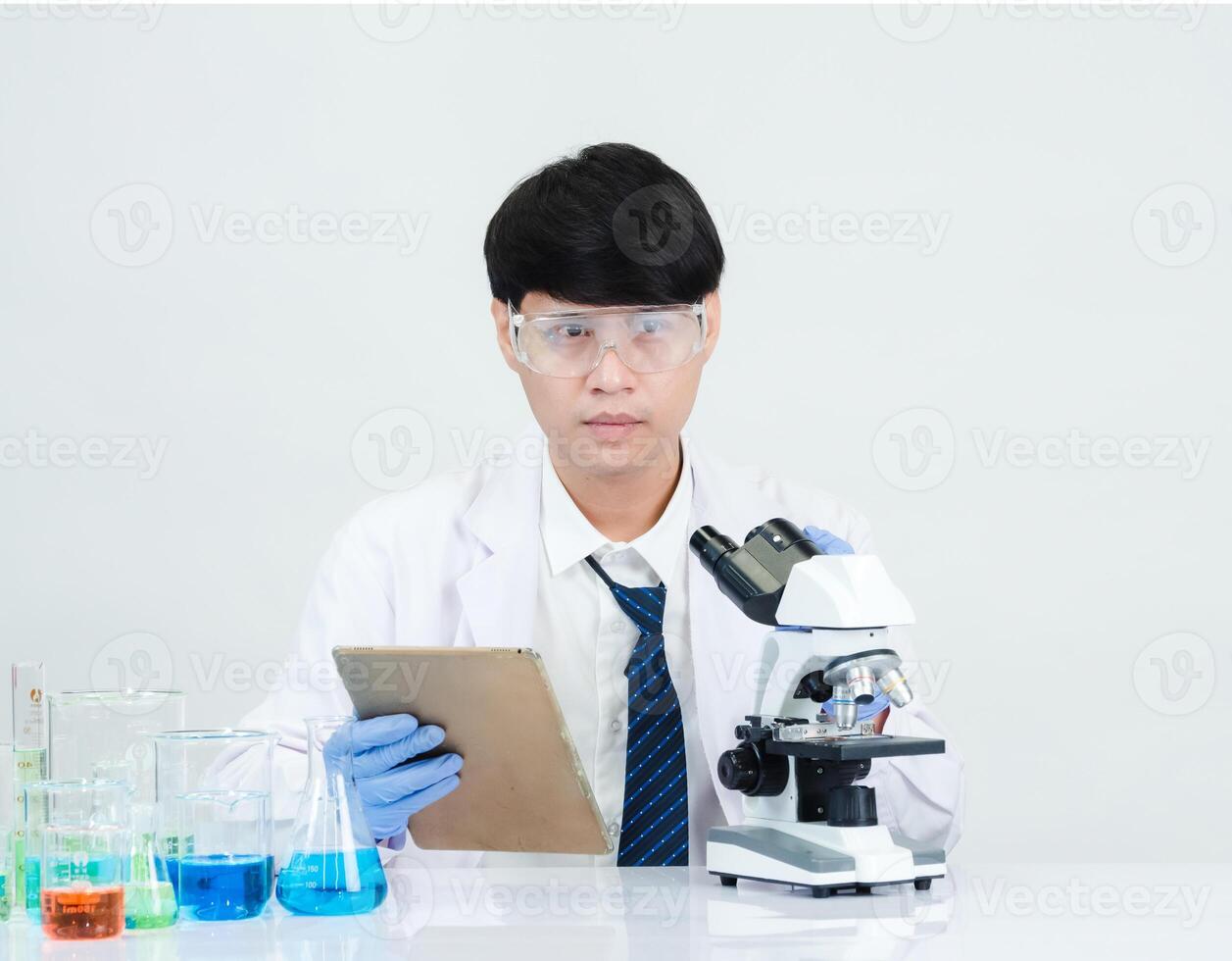 retrato ásia homem aluna cientista médico dentro camisa vestido 1 pessoa trabalho trabalho plantar olhando mão segurando ao controle microscópio em branco mesa Vejo a resultados do científico experimentos dentro laboratório foto