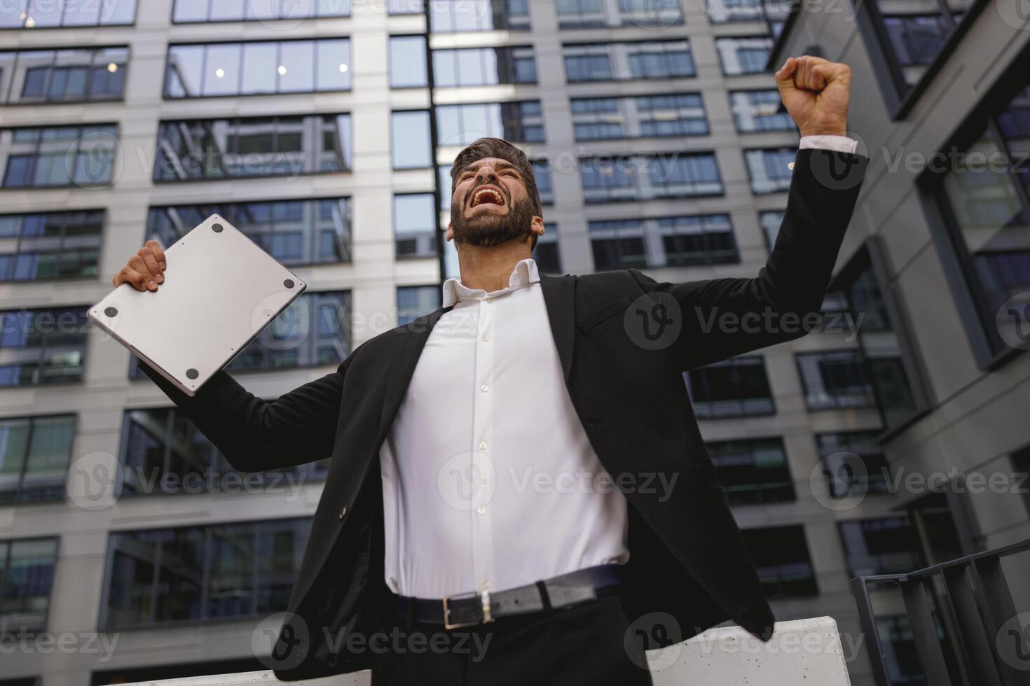 homem de negocios com computador portátil em pé em escritório terraço e elevado punho é satisfeito do acabado projeto foto