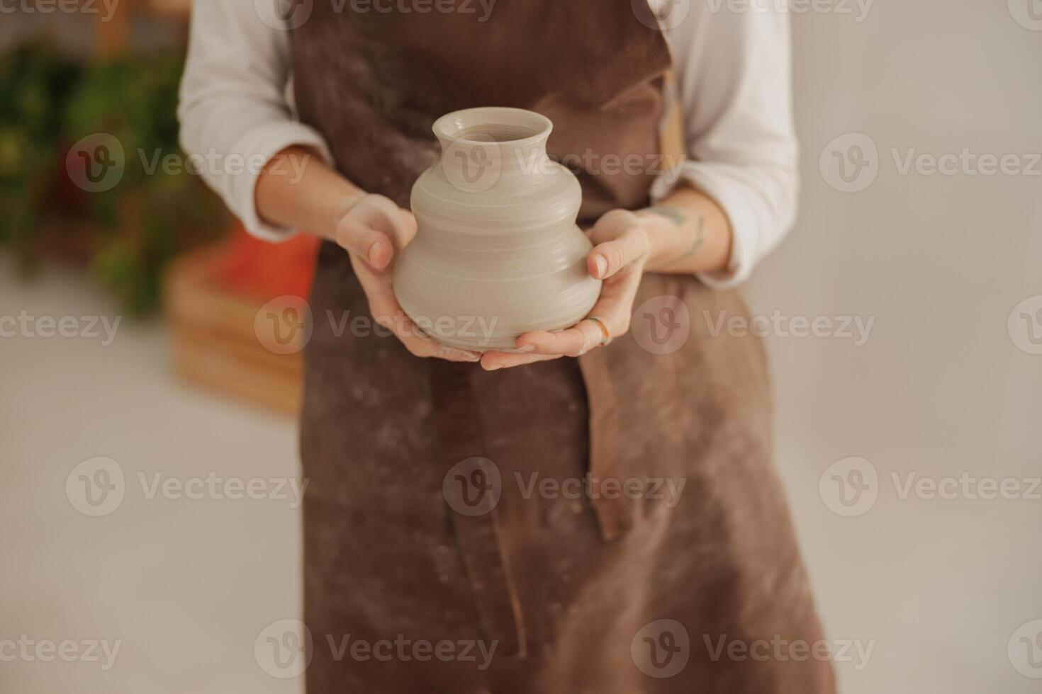 fechar acima do oleiro vestindo avental segurando não disparado argila vaso enquanto em pé dentro cerâmica estúdio foto