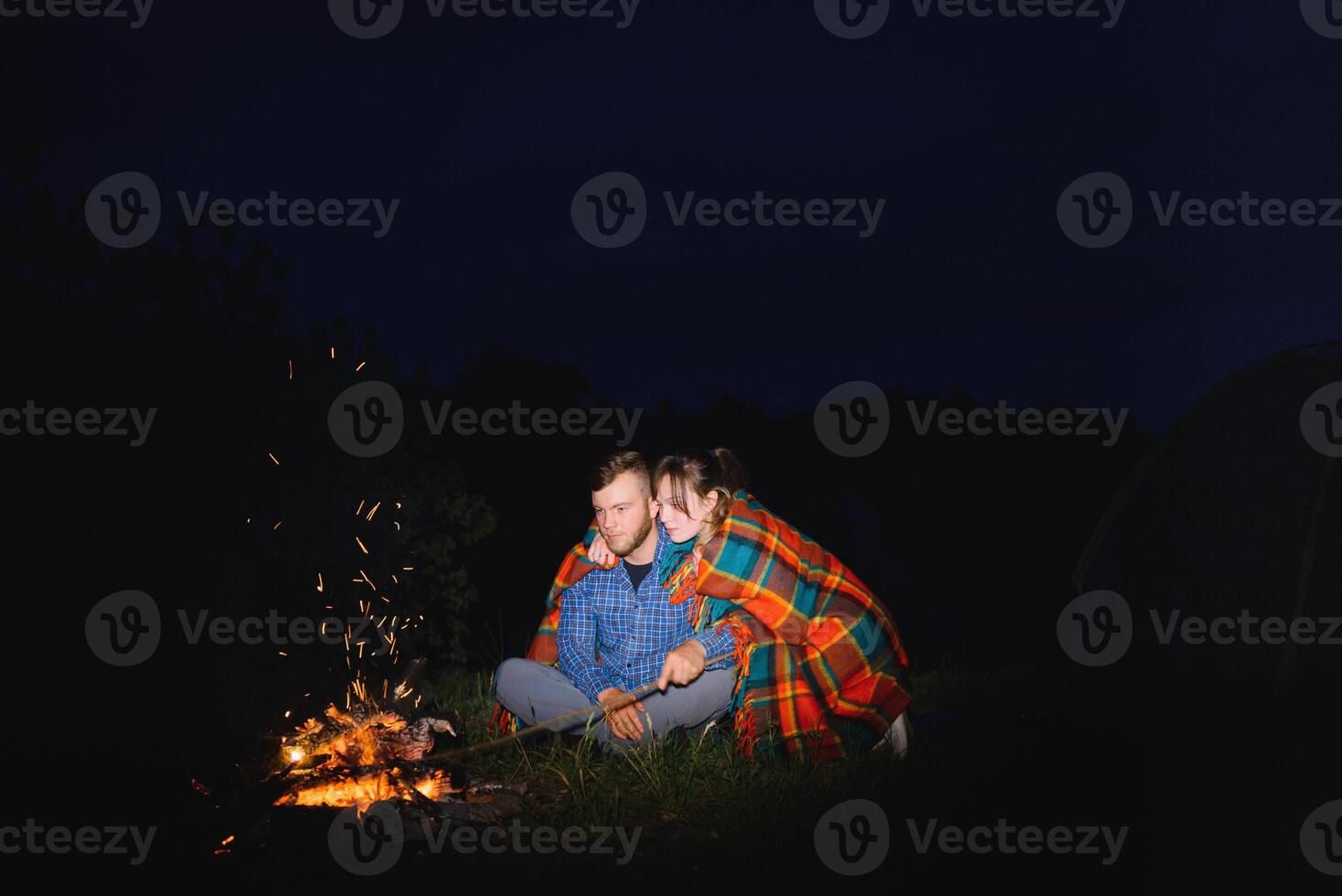 jovem casal homem e mulher viajantes sentado perto brilhando turista barraca, queimando fogueira, em a topo do montanha, desfrutando lindo Visão do noite céu. foto