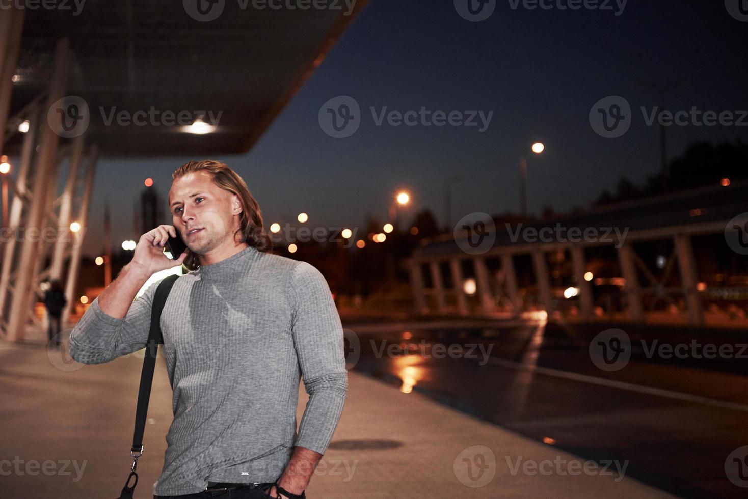 toda a atenção na conversa sobre reunião. jovem elegante andando pela rua à noite perto da estrada e conversando ao telefone foto