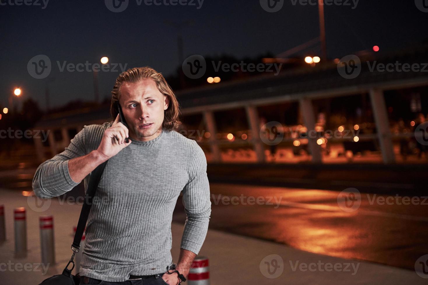 tendo lidar com algumas coisas. jovem elegante andando pela rua à noite perto da estrada e conversando ao telefone foto