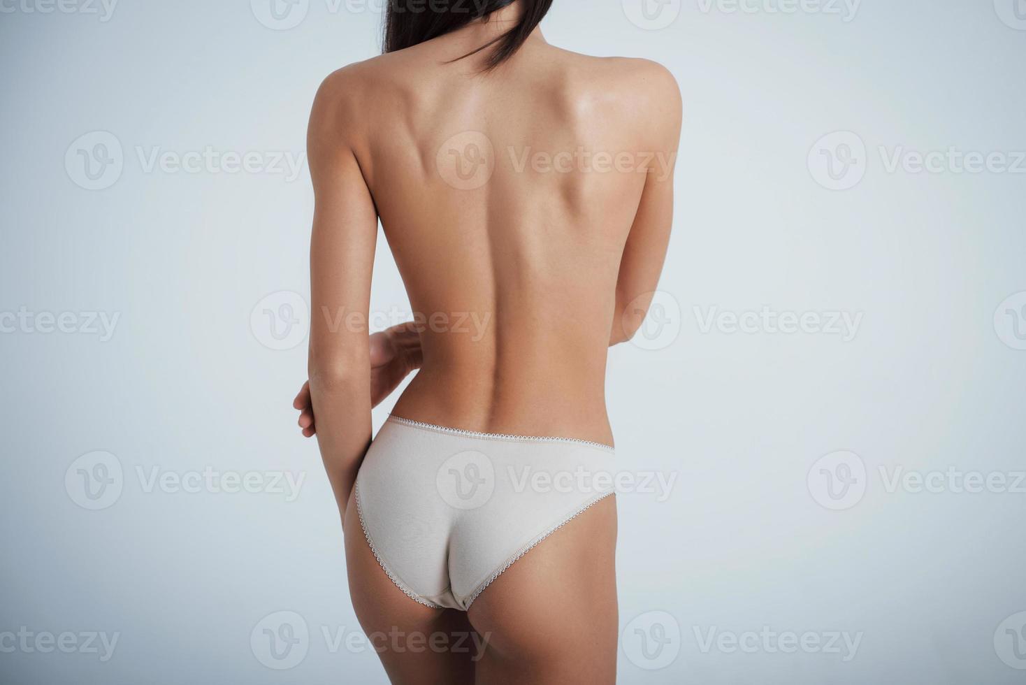 garota com corpo perfeito em cueca branca, virando-se de costas para o fundo branco no estúdio foto