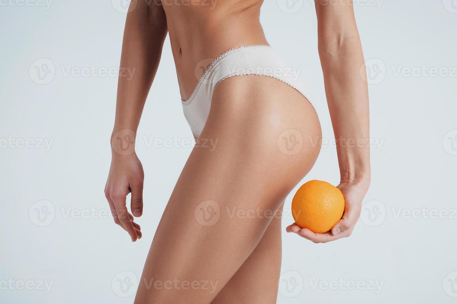 garota com corpo tipo fitness em pé no fundo branco com laranja na mão foto