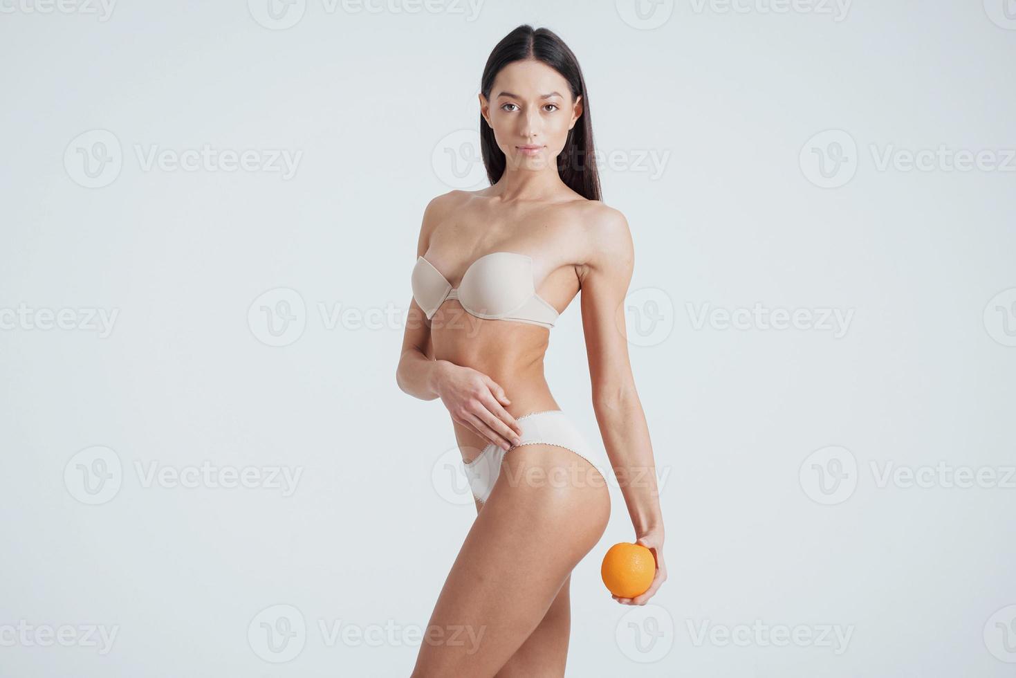 virando o lado esquerdo. garota de corpo fitness em cueca posando para uma foto com frutas nas mãos