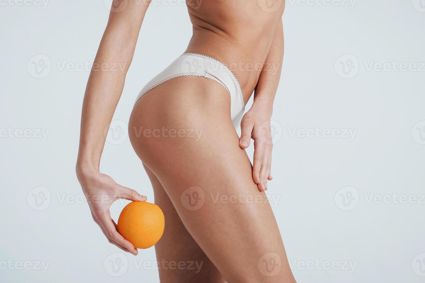 foto de garota de cueca virando o lado direito do corpo para a câmera e segurando uma laranja na mão