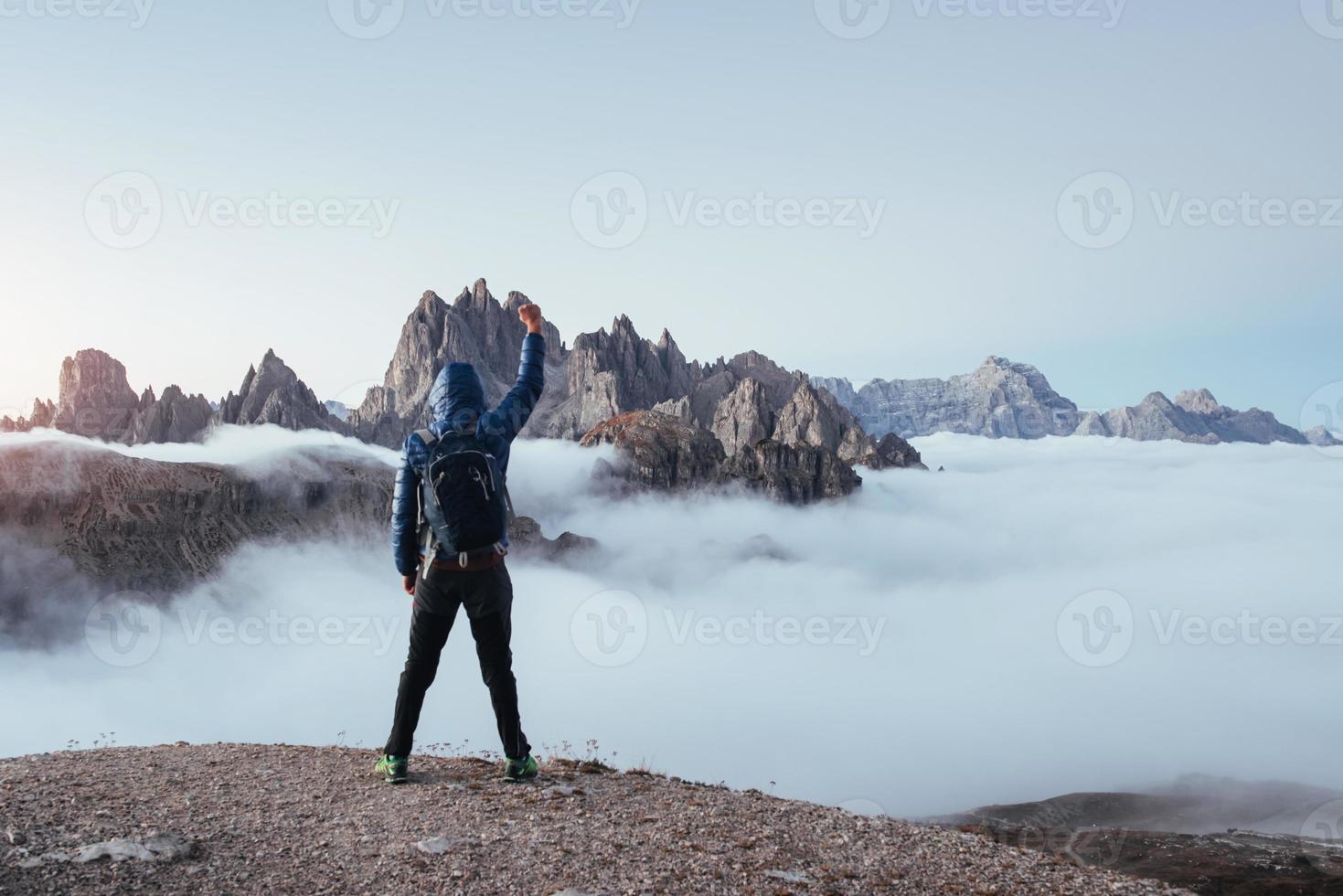 extremos em pé na borda. homem turístico levantou as mãos sobre as belas montanhas cheias de nevoeiro à luz do dia foto