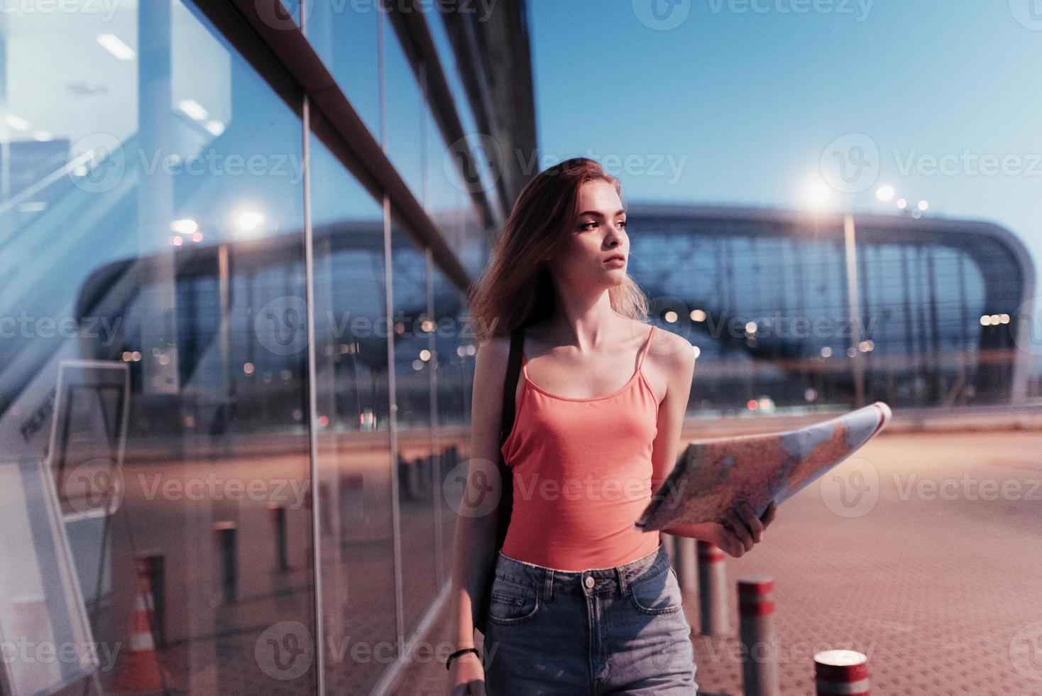 jovem atraente olhando para o lado, segurando o mapa na mão e caminhando perto do prédio da empresa foto