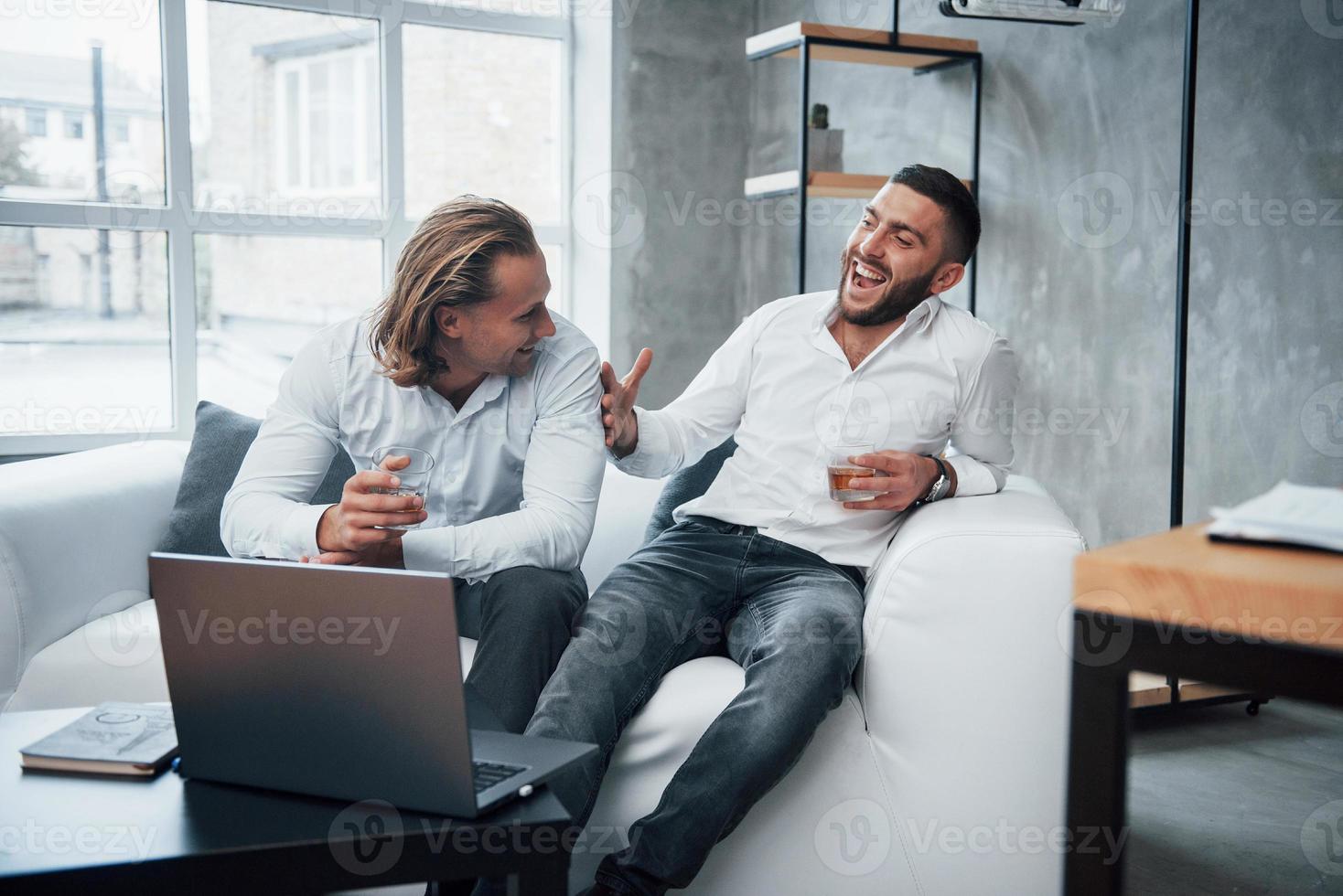 homem de cabelos curtos gosta da ideia. dois empresários sentados em frente a um laptop falando sobre seus planos foto