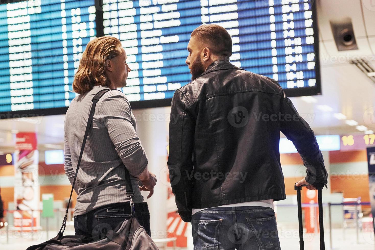 foto de dois camaradas situados no aeroporto perto do sistema de exibição de informações de voo