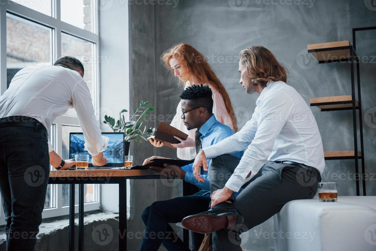 usando laptop. grupo de funcionários multirraciais em roupas formais conversando sobre tarefas e planos foto