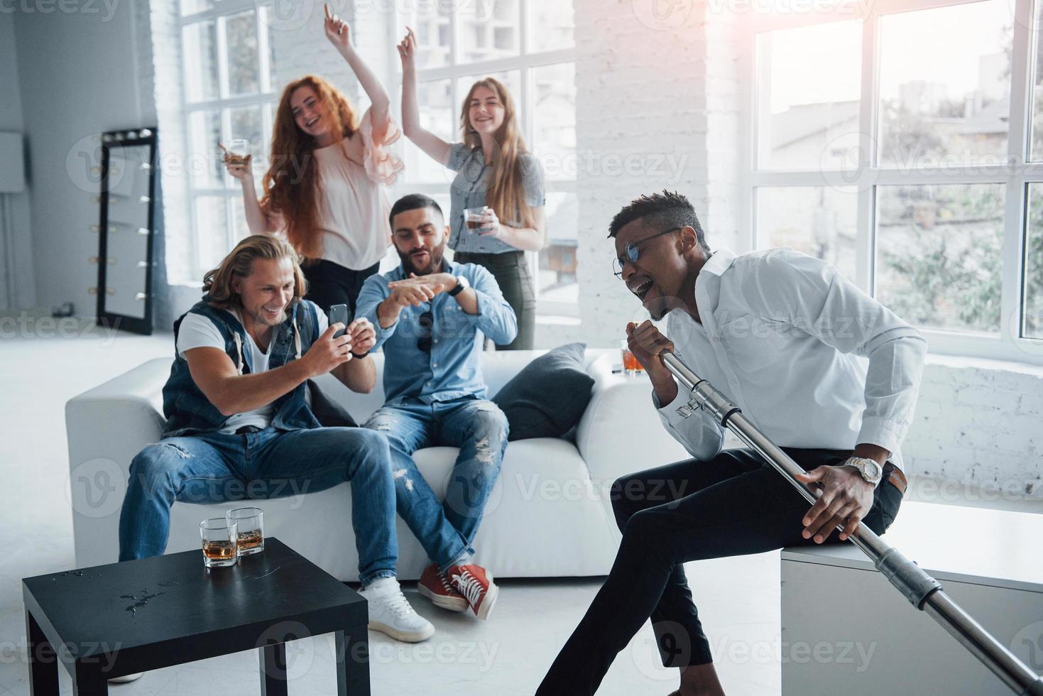 cara afro-americano incrível na frente das pessoas começa a multidão. amigos decidem relaxar cantando suas canções favoritas foto