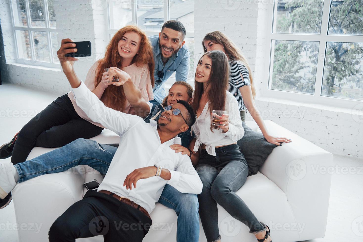 conceito de lazer. jovens amigos alegres se divertindo e bebendo no interior branco foto