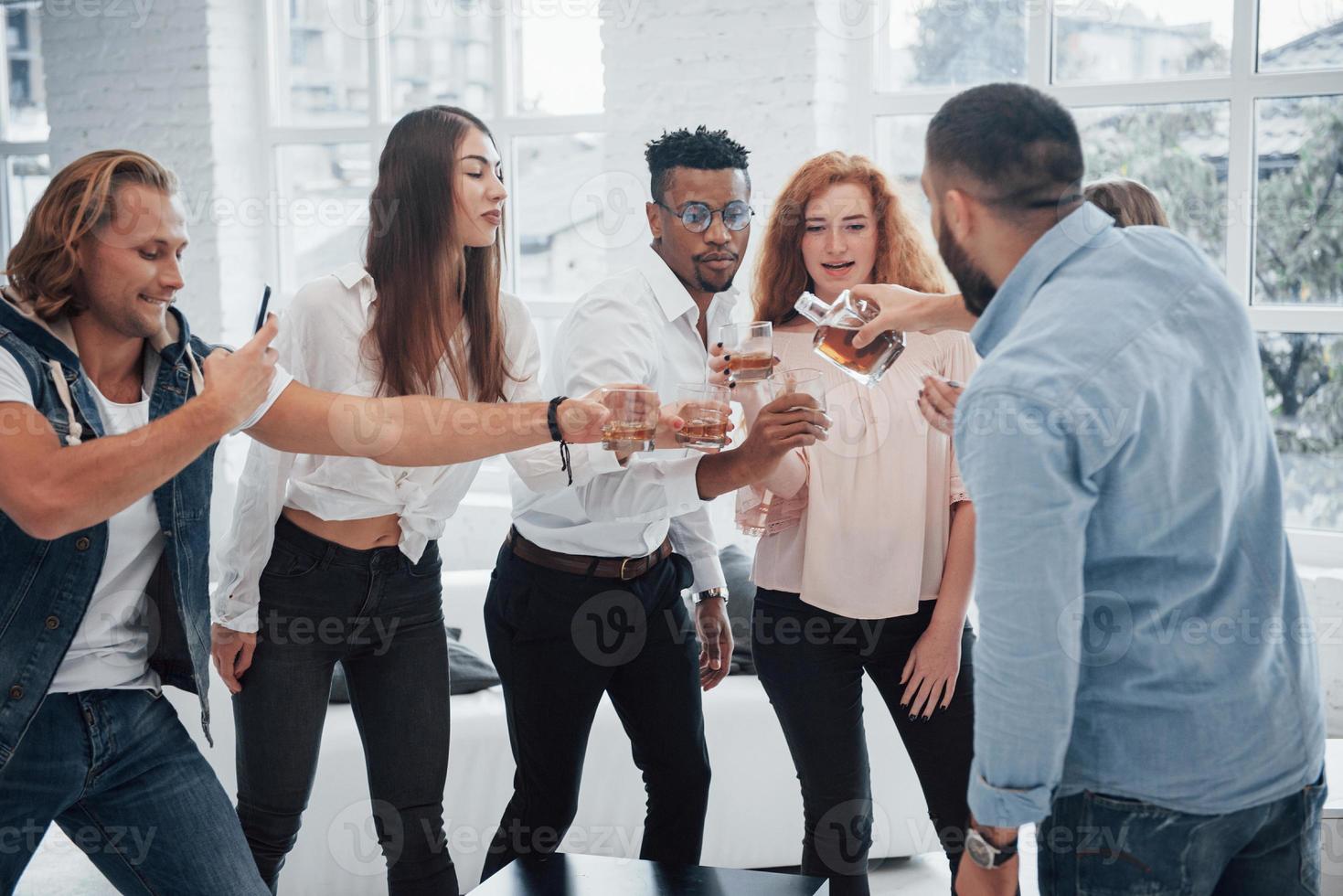 vamos capturar esse momento. jovens amigos alegres se divertindo e bebendo no interior branco foto