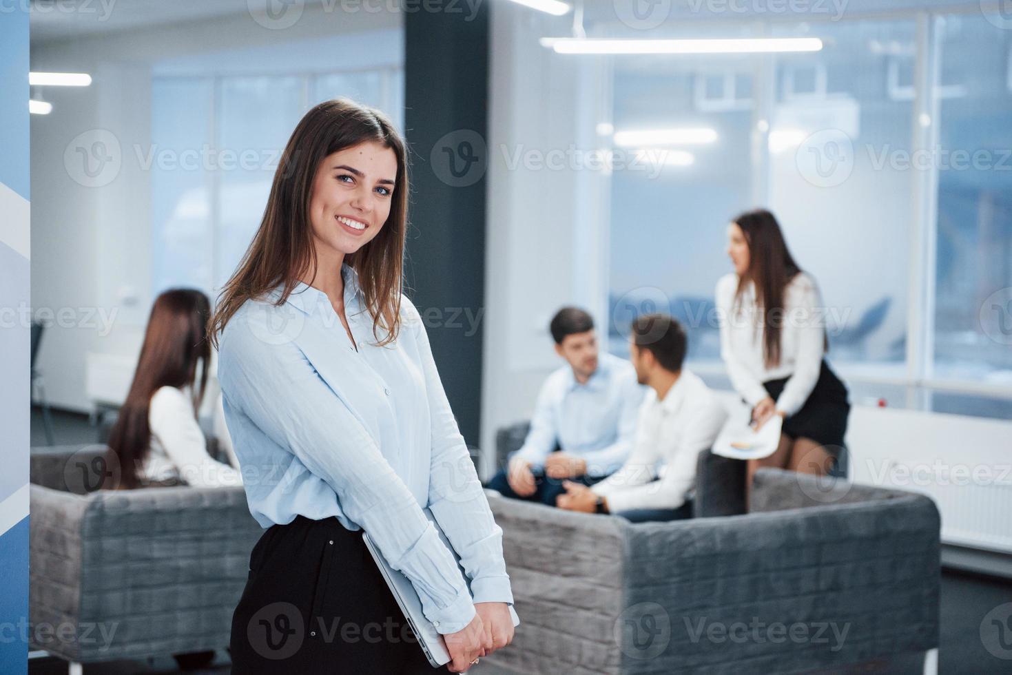 laptop nas mãos. retrato de uma jovem no escritório com funcionários no fundo foto