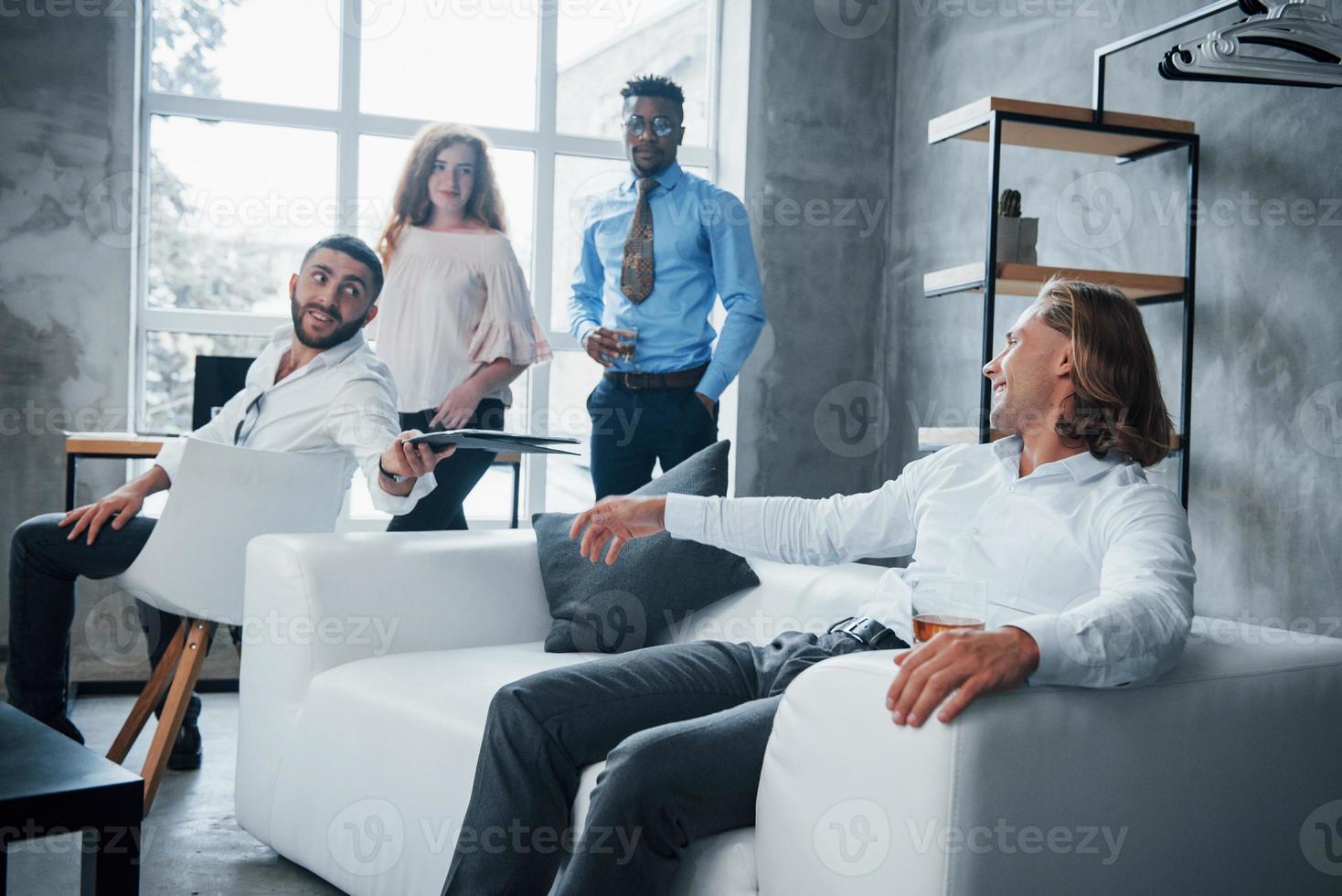 homem com cabelo curto deseja compartilhar seus resultados com outro cara. grupo de funcionários multirraciais em roupas formais conversando sobre tarefas e planos foto