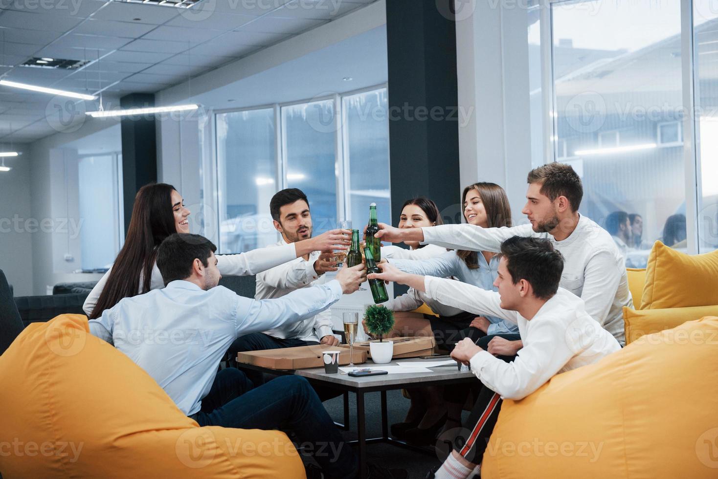 celebrando negócio de sucesso. jovens trabalhadores de escritório sentados perto da mesa com álcool foto