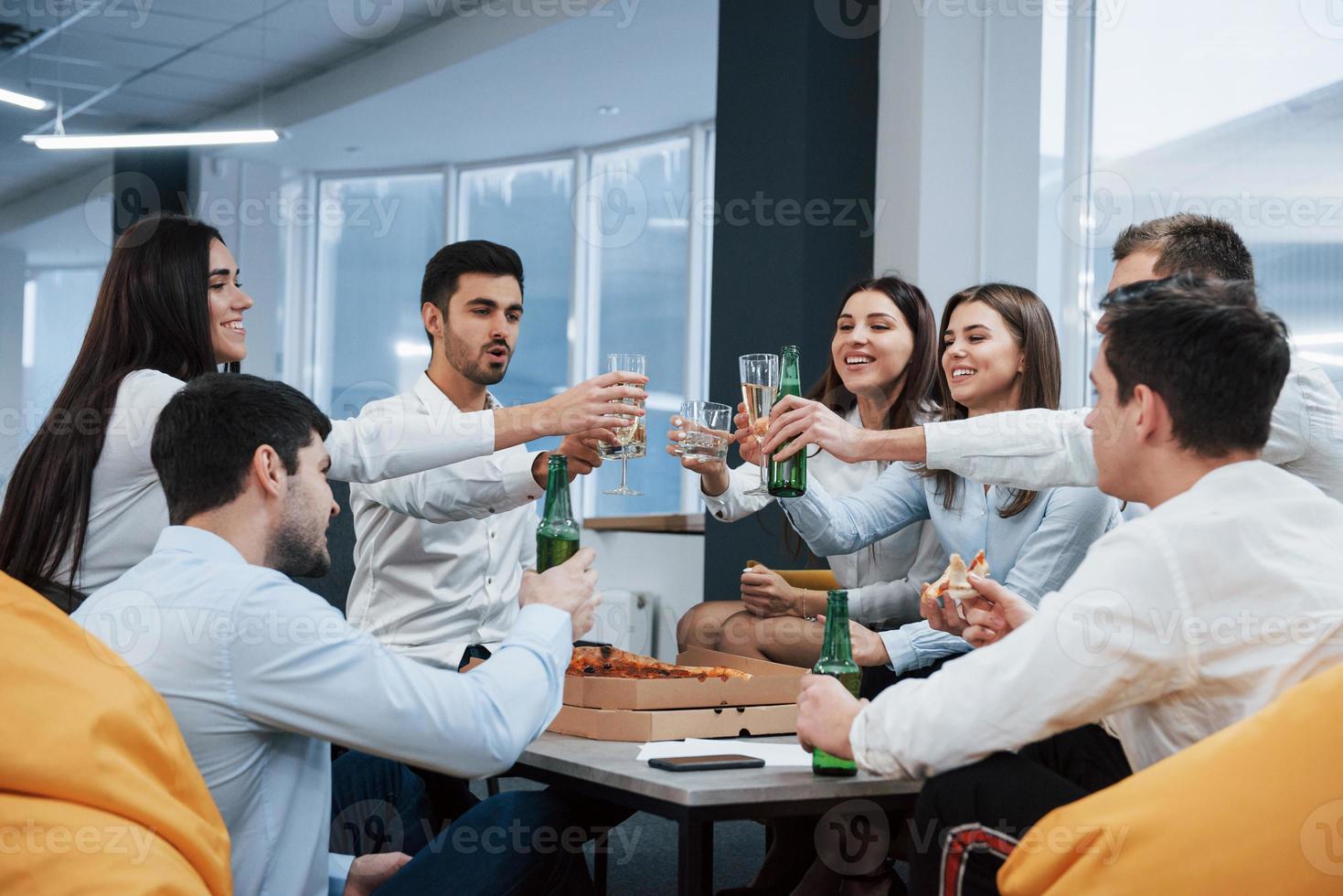 para o nosso futuro. celebrando negócio de sucesso. jovens trabalhadores de escritório sentados perto da mesa com álcool foto