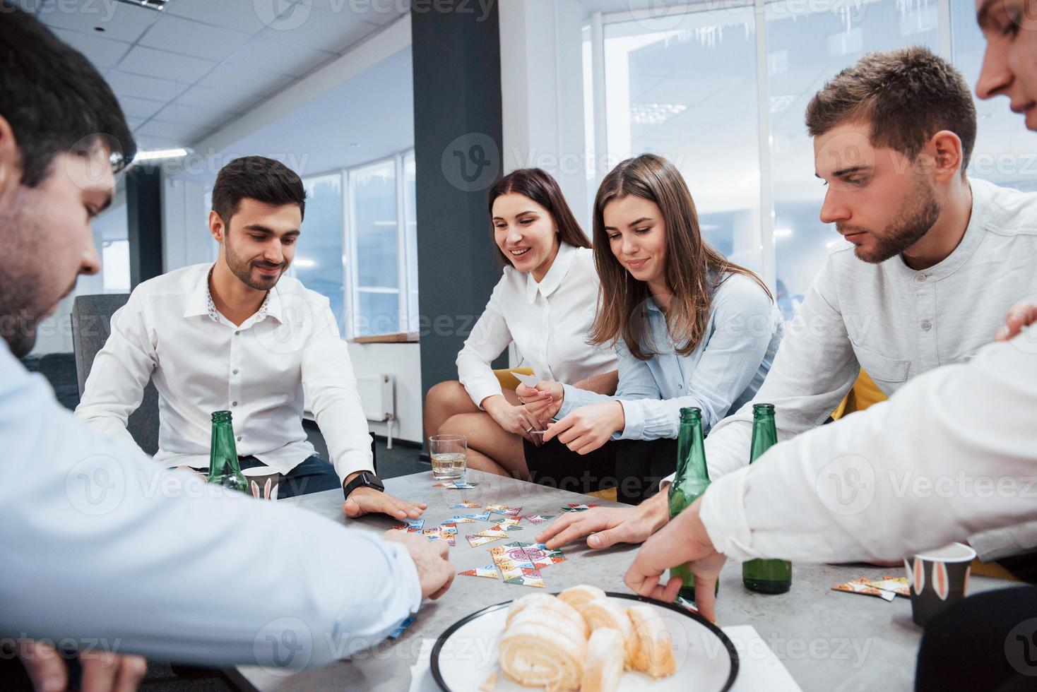 descansando depois de um dia difícil. relaxando com o jogo. celebrando negócio de sucesso. jovens trabalhadores de escritório sentados perto da mesa com álcool foto