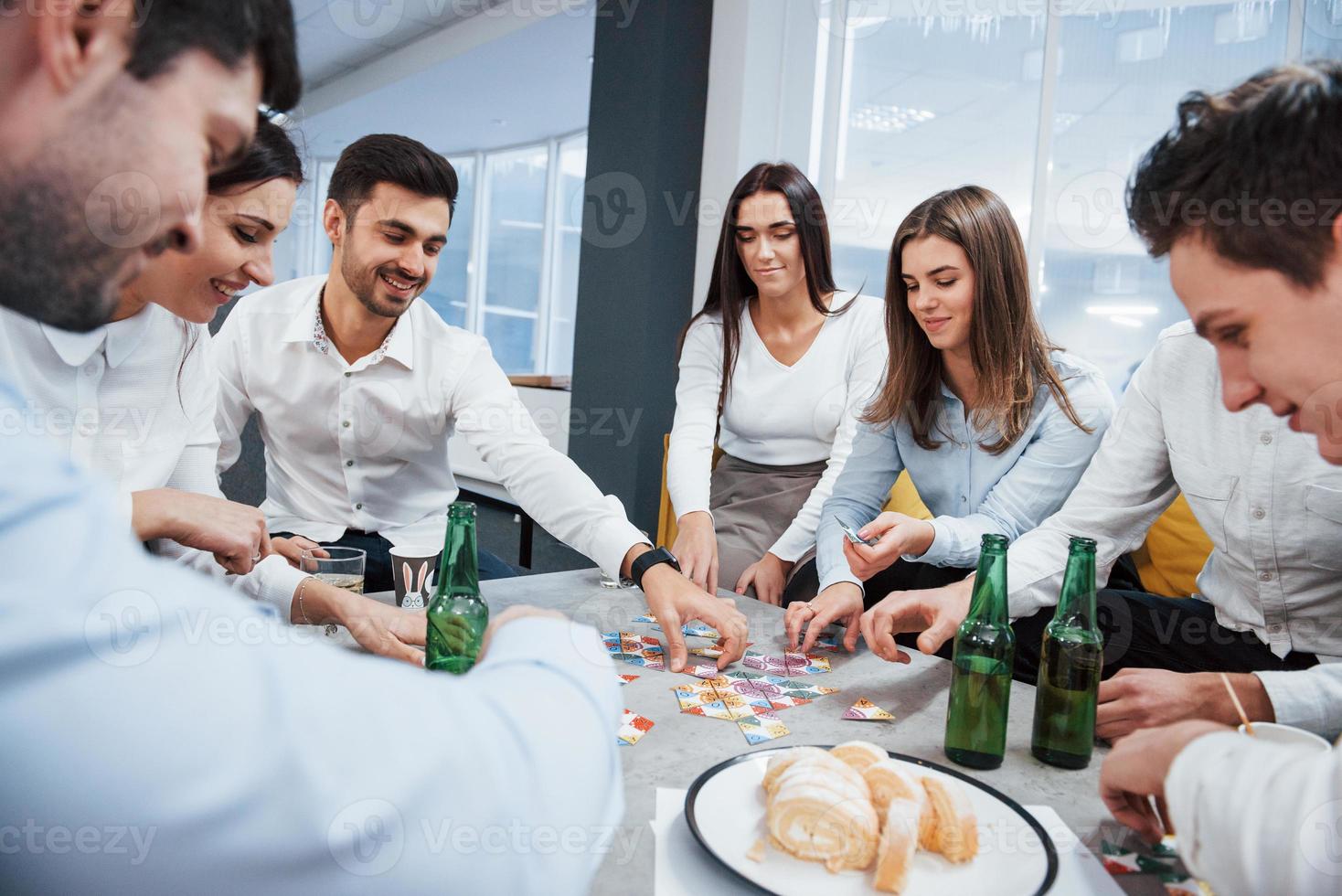 reunião amigável. relaxando com o jogo. celebrando negócio de sucesso. jovens trabalhadores de escritório sentados perto da mesa com álcool foto
