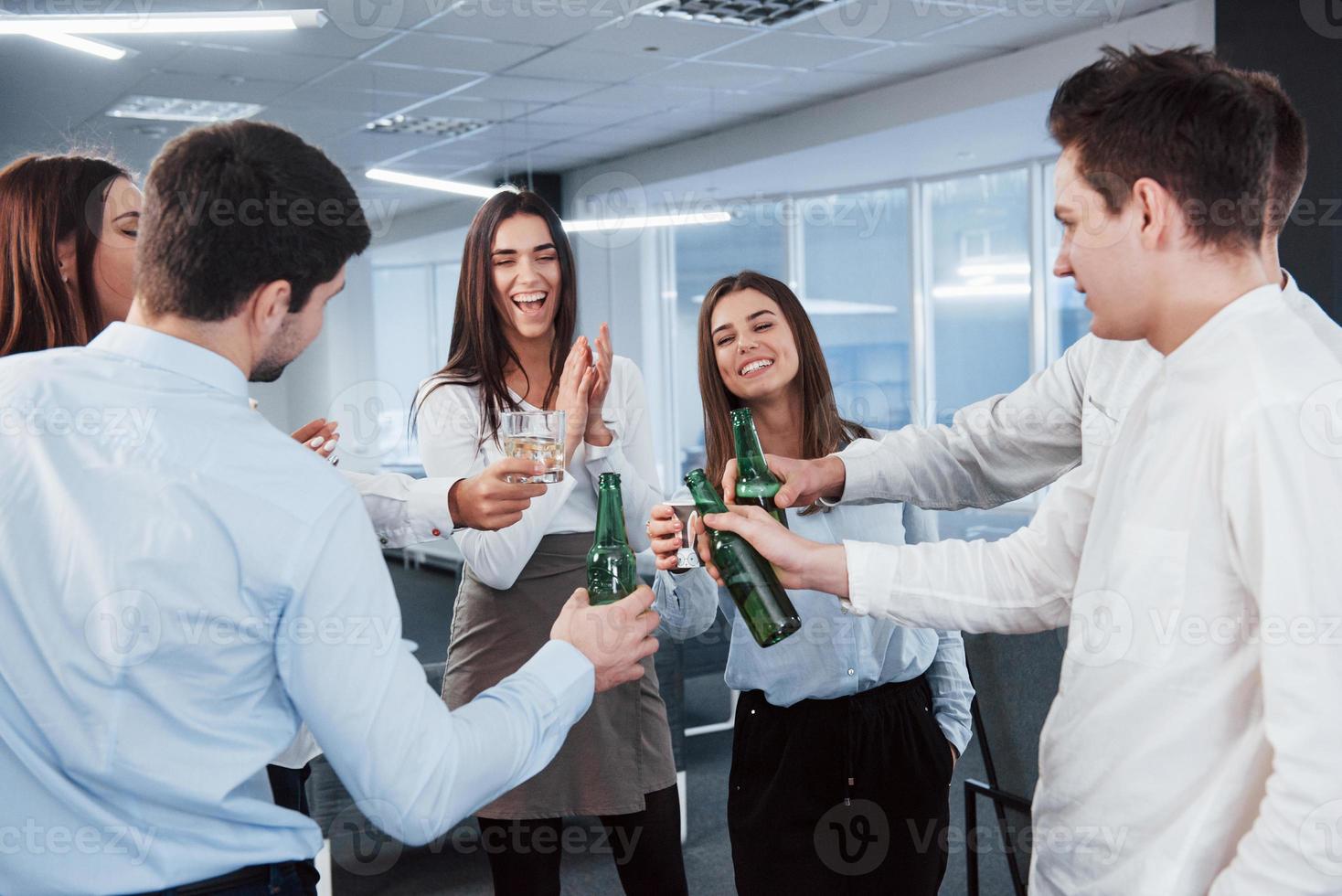 em pé e batendo nas garrafas e nos vidros. no escritório. jovens celebram seu sucesso foto
