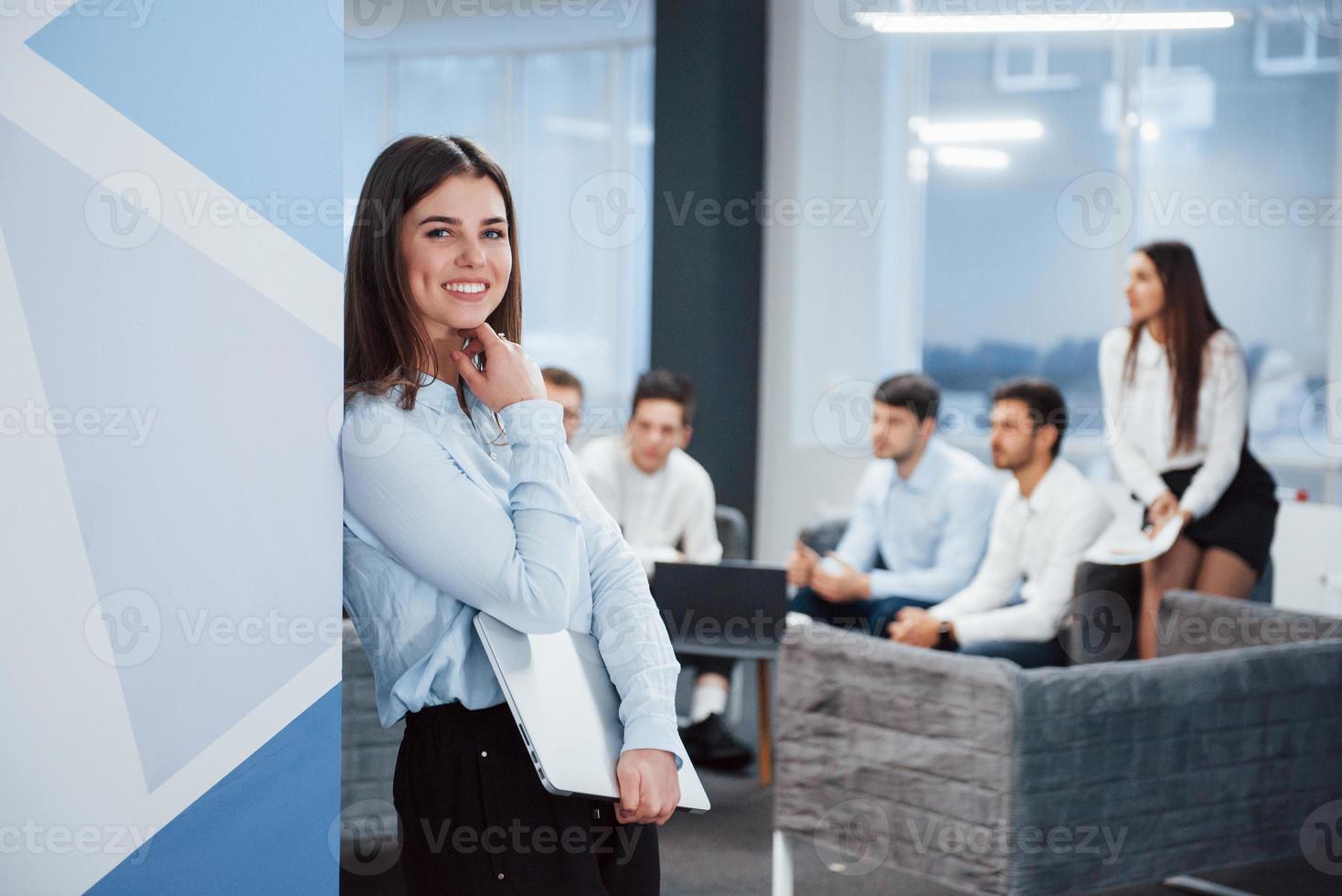 contando com a parede. retrato de uma jovem no escritório com funcionários no fundo foto