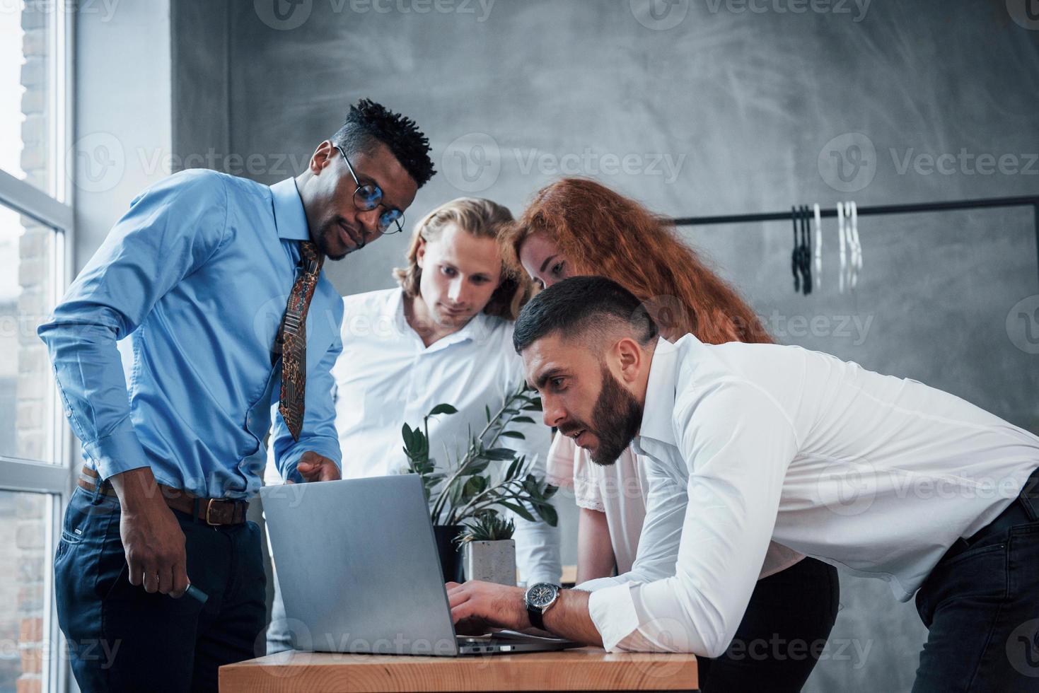 o cara afro-americano mostra o que fazer. quatro jovem empresário trabalhando no plano usa notebook foto