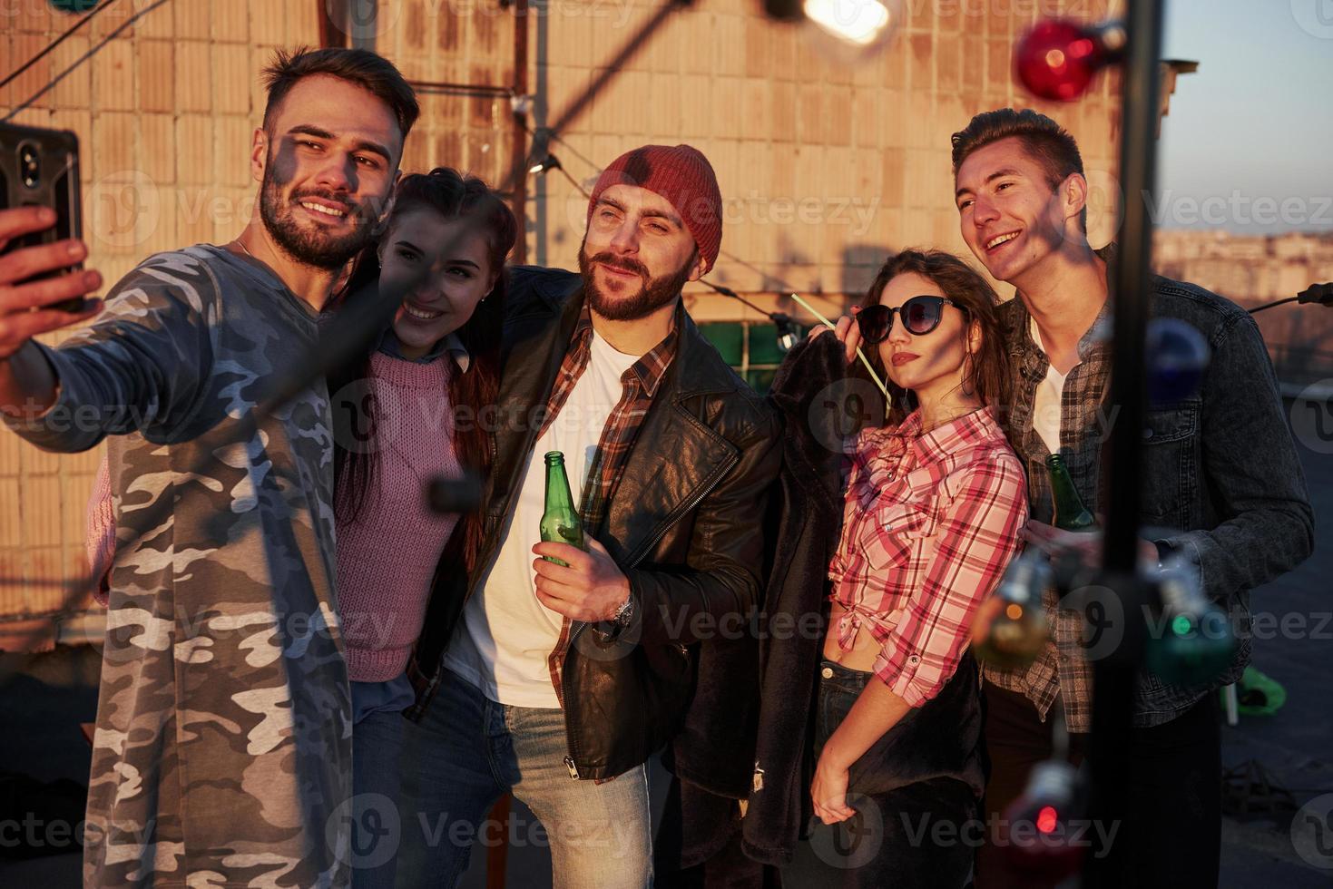 hora de selfies para um grupo de amigos positivos fica no telhado com uma parede atrás foto