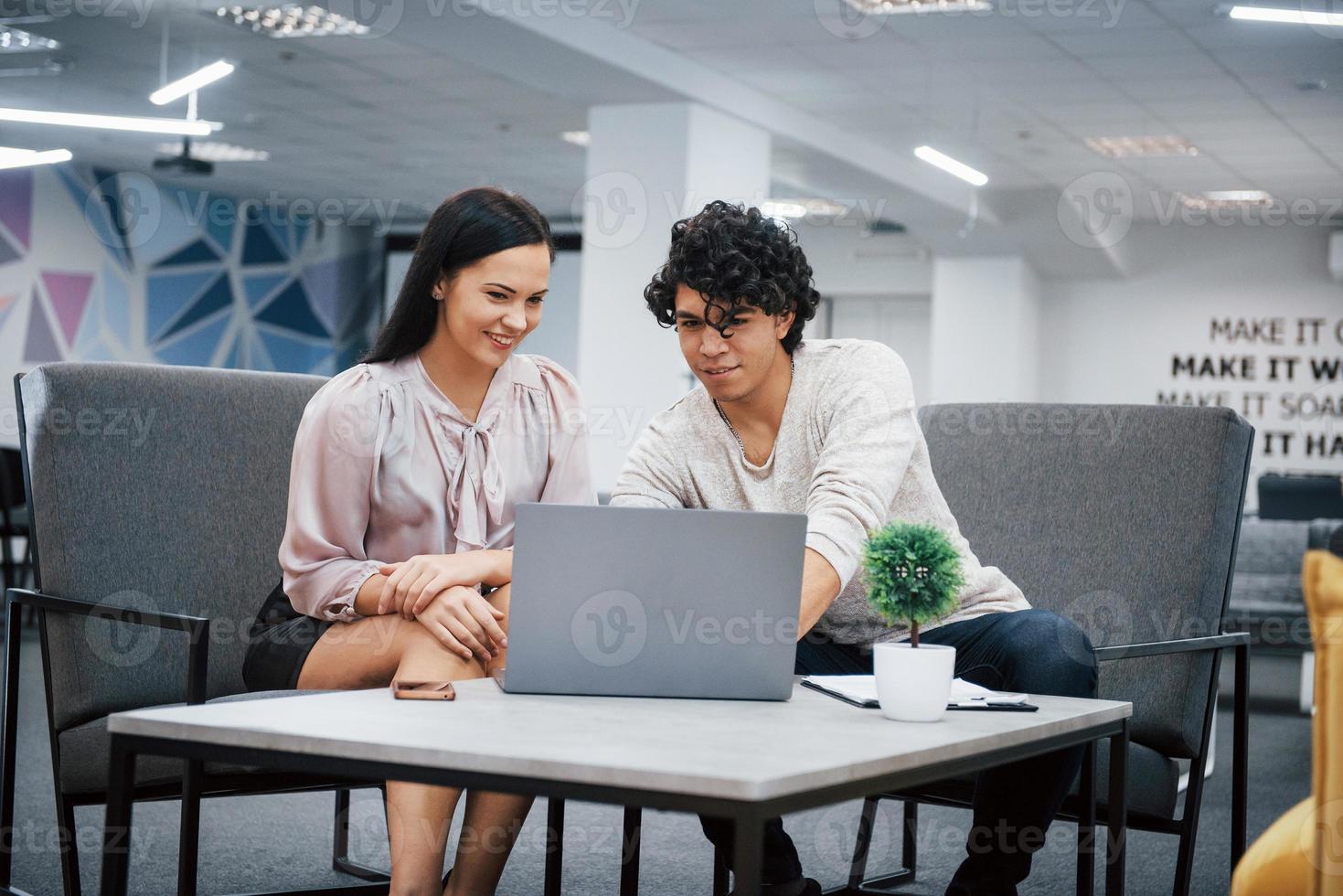 trabalhando usando laptop. cara encaracolado e menina morena discutem os detalhes do contrato em um escritório moderno foto