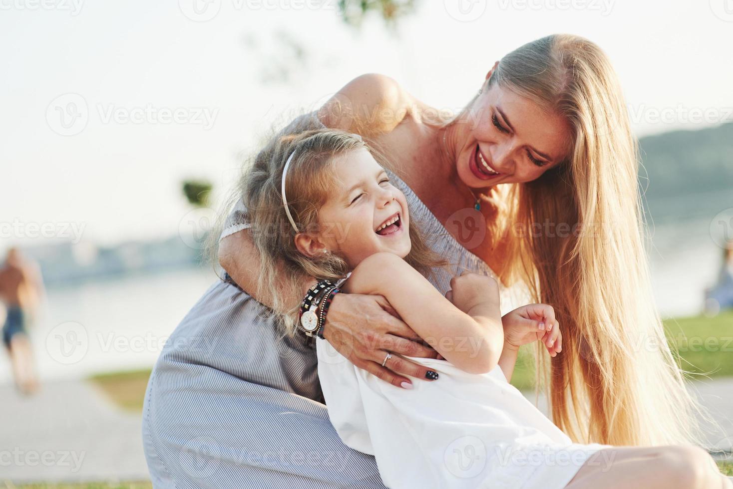 todo mundo está rindo. foto de uma jovem mãe e sua filha se divertindo na grama verde com um lago ao fundo