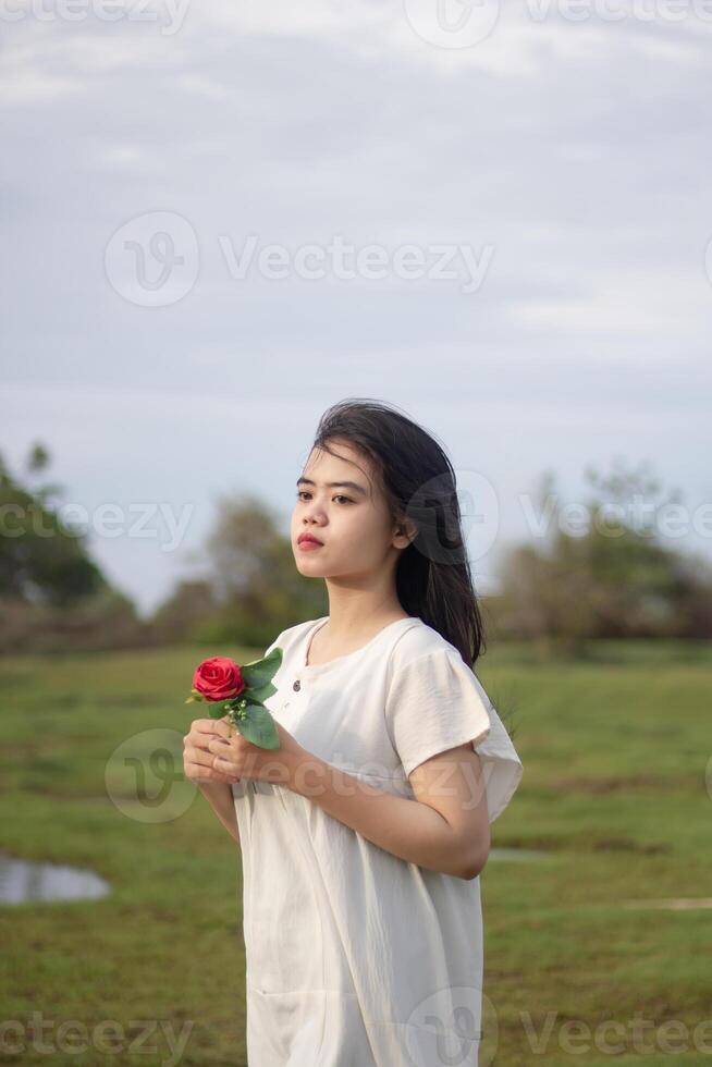 retrato do uma bonita jovem mulher vestido dentro branco vestir segurando rosa flores foto