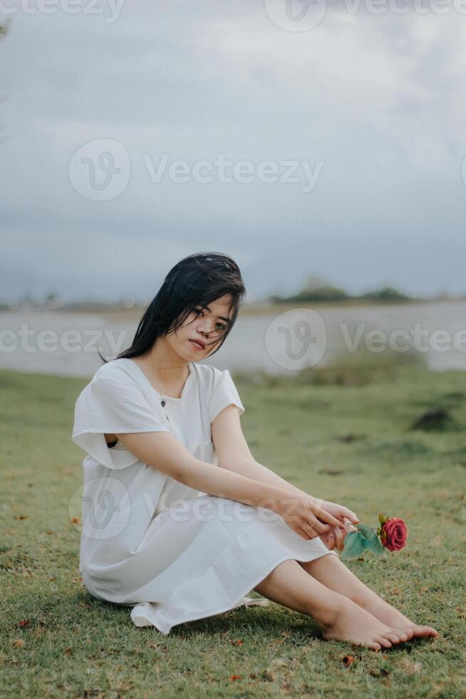 retrato do uma bonita jovem mulher vestido dentro branco vestir segurando rosa flores foto