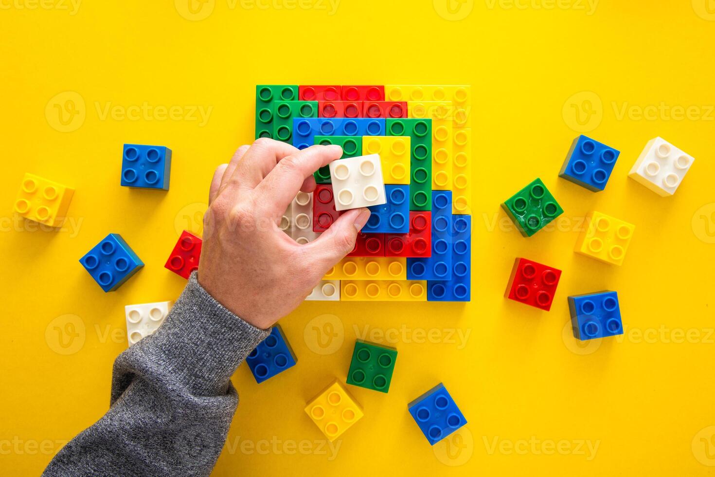 mão empilhamento acima a colorida plástico quadra em amarelo fundo foto