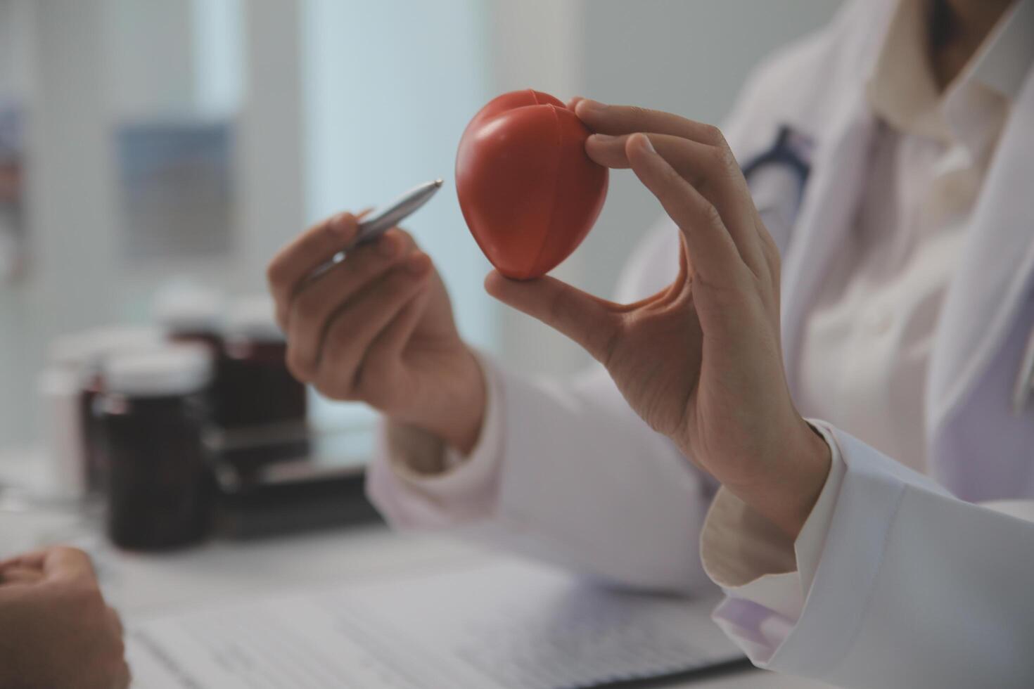 mãos do médico mulher segurando vermelho coração, mostrando símbolo do amor, humano Apoio, suporte para paciente, promovendo médico seguro, cedo checar para assistência médica, cardiologista ajuda. fechar acima do objeto foto