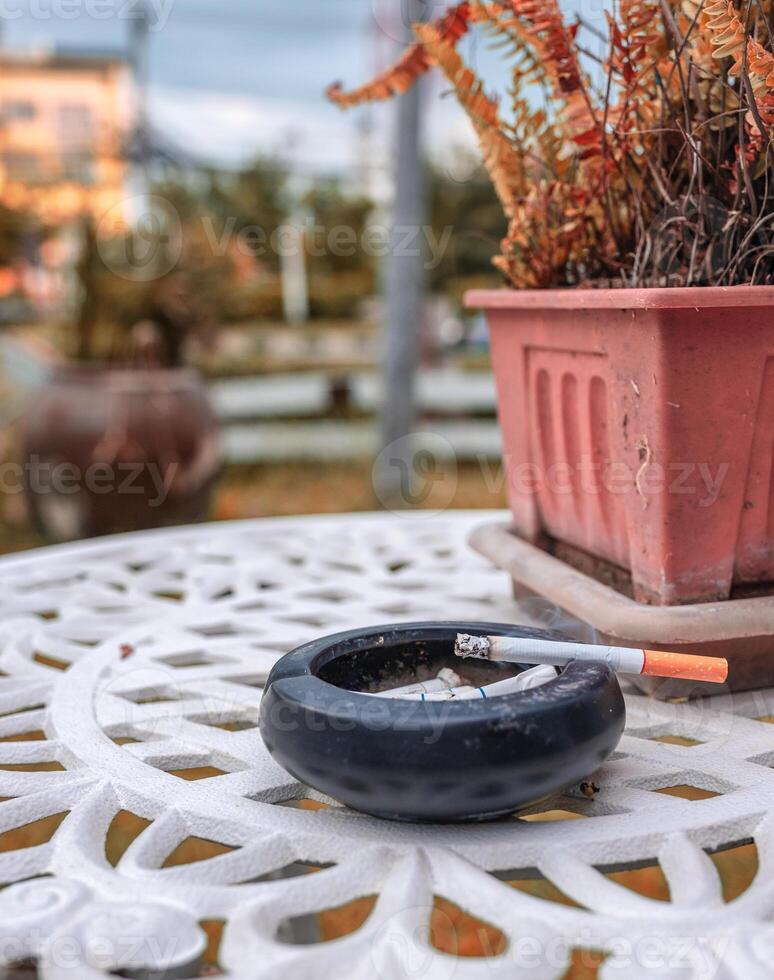 cigarro queimando com fumaça em cerâmico cinzeiro e seco plantar decoração foto