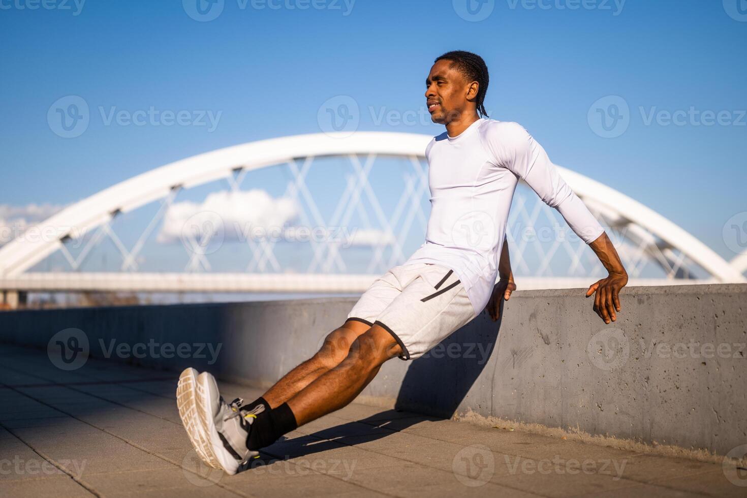 jovem afro-americano homem é exercício dentro a cidade. ele é fazendo marcha ré flexões. foto