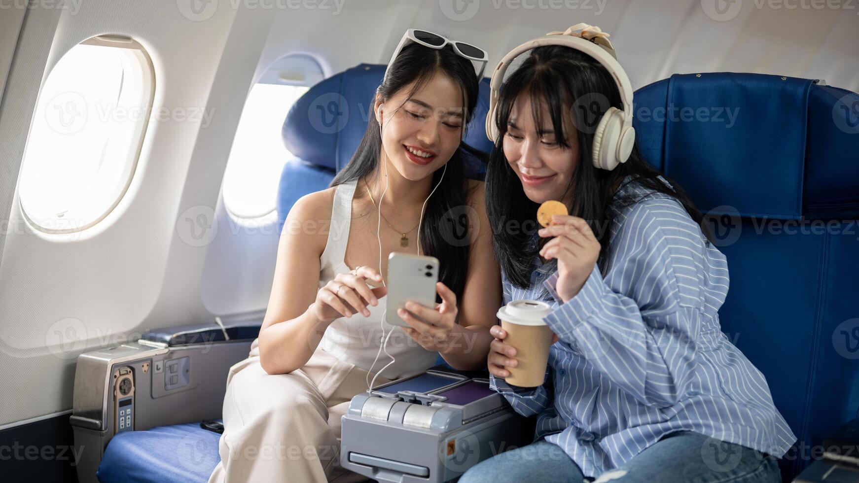 dois feliz jovem ásia fêmea amigos passageiros estão desfrutando falando juntos durante a voo. foto